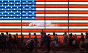 People walking in front of a US flag