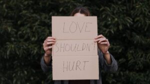 a woman holding a cardboard with the caption LOVE SHOULDNT HURT